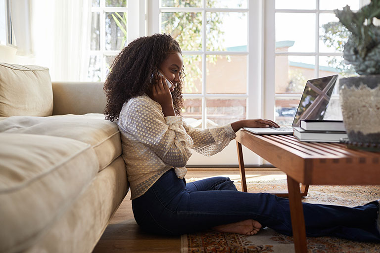 Young woman on phone with laptop in living room