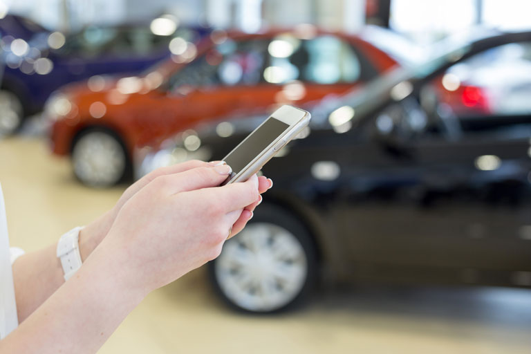 A person holding a smartphone at a car dealership.