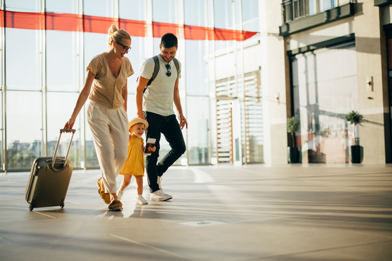 A family of three walking through an airport. The little girl is cute with a yellow dress and she is holding a passport. 