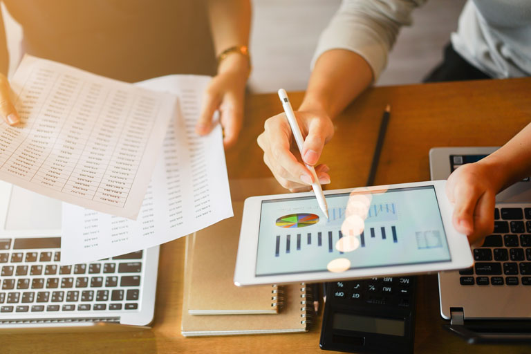 Two people holding financial papers and a tablet with graphs on it.