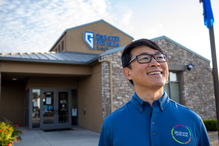 A smiling man with a Greater Nevada polo standing in front of a Greater Nevada Credit Union branch.