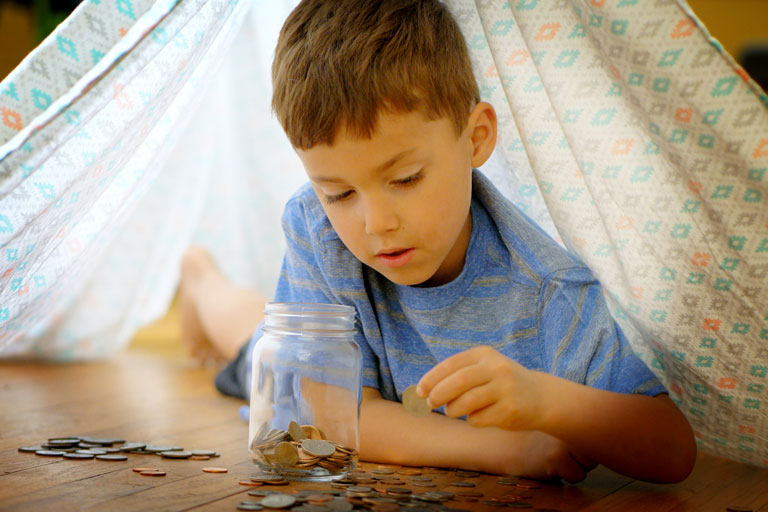 Child under a blanket fort counting money. 