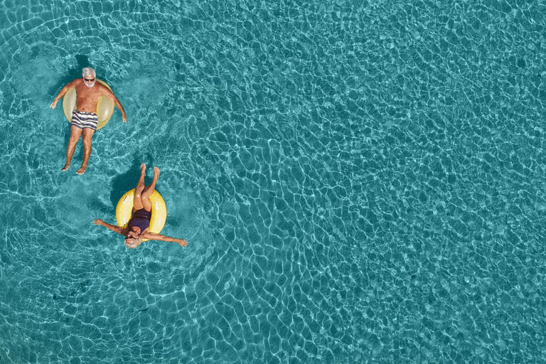 An older man and woman floating on innertubes in rippled water.   