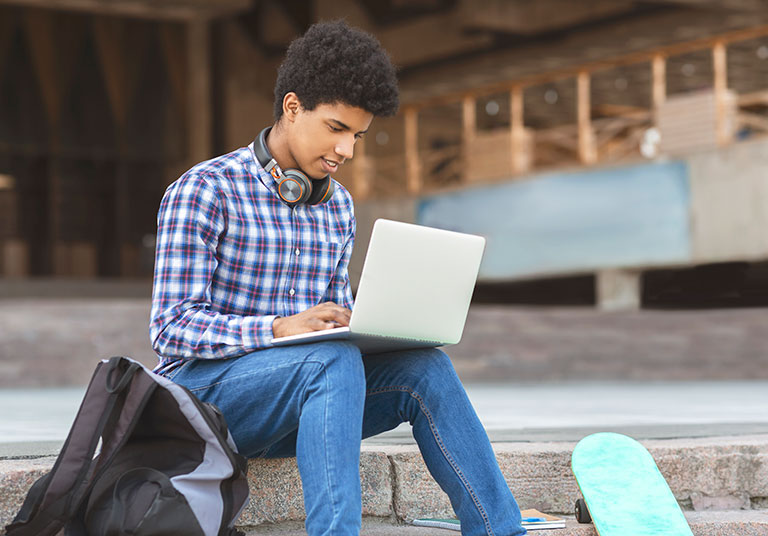 Male teen on laptop outside