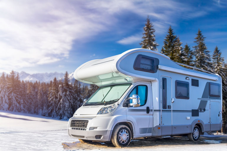 RV outside in winter in front of a field of pine trees.