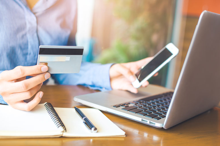 Woman looking at her laptop holding a credit card in her right hand and a cellphone in her left hand.