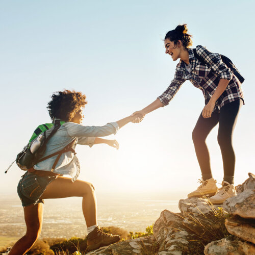 Two women hiking helping each other up the mountain