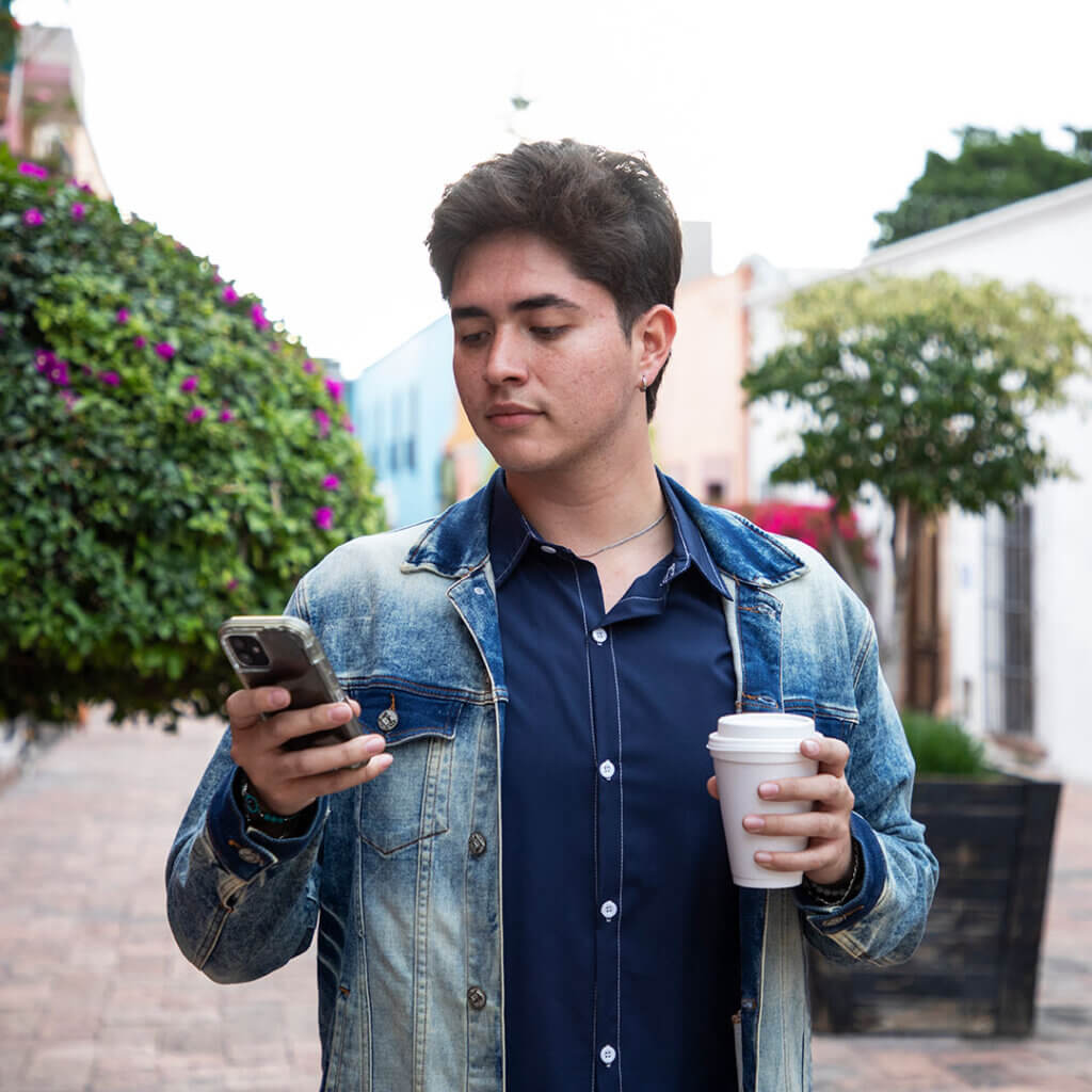 Young man holding smartphone and coffee while outside