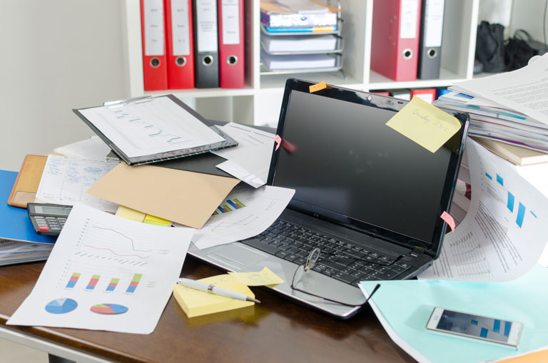 A messy desk with a laptop and a bunch of papers.