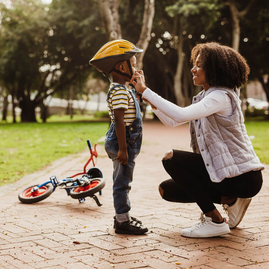 Mom fastening helmet on her son to ride a bike