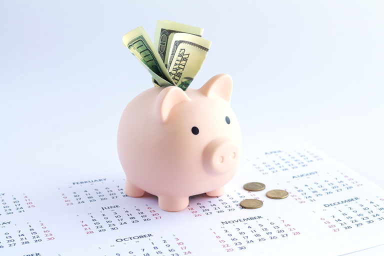 A piggy bank with $100 bills sticking out the top on a calendar.