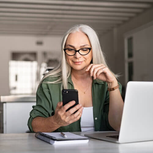 Woman looking at smartphone while also on laptop