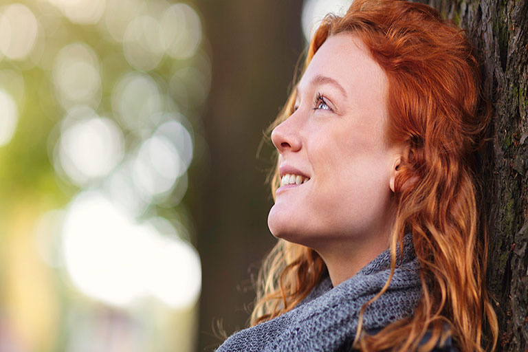 happy woman smiling while leaning against tree