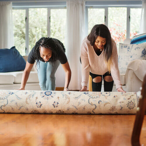 two women rolling out a rug at home