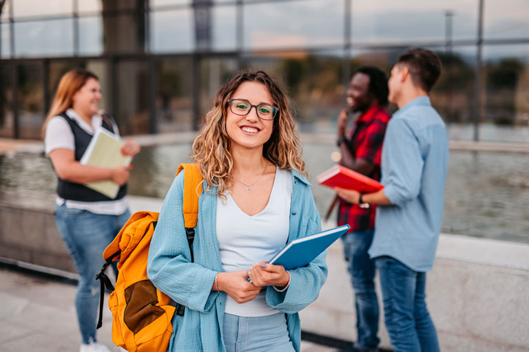 Young woman holding backpack and book with other friends behind