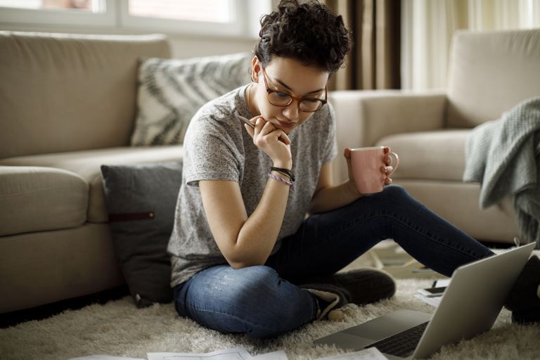 Young woman paying bills on living room floor