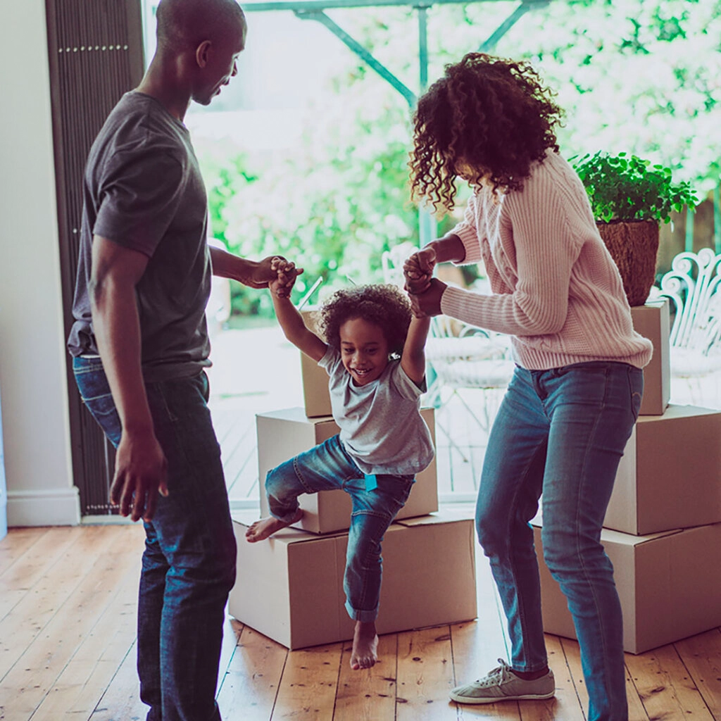 A family happily swinging their child with moving boxes in the background