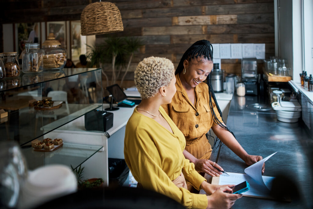 Small business owners talking and discussing the performance of their coffee shop. Black female entrepreneurs in a partnership collaborating and planning growth together inside their cafe or shop