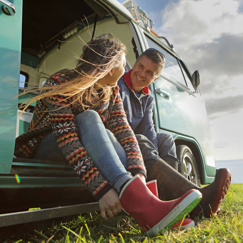 Man and woman putting shoes on while sitting at a VW bus outdoors