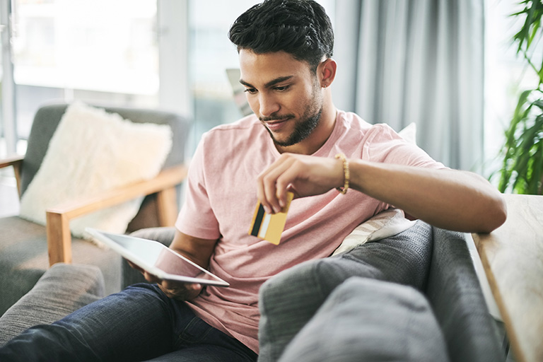 young man using a credit card and digital tablet on the sofa at home