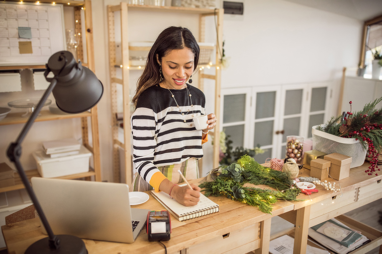 Working woman at gift shop. She is checking online shop with laptop and using mobile phone to receive new orders from customer.