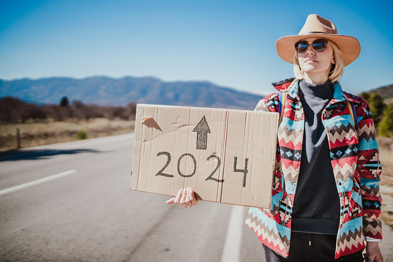 Woman hitchhiking and holding a cardboard sign thinking about financial health for 2024.