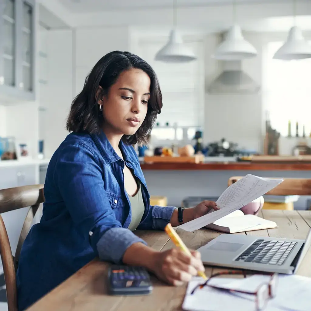 A woman in her kitchen using the debt consolidation calculator while look at bills