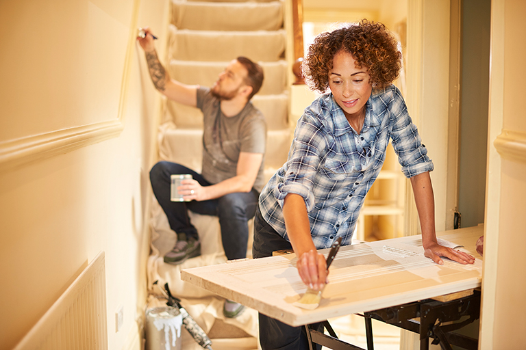 A couple painting a door and a wall in their home. Home improvements are an excellent use of a HELOC Loan.