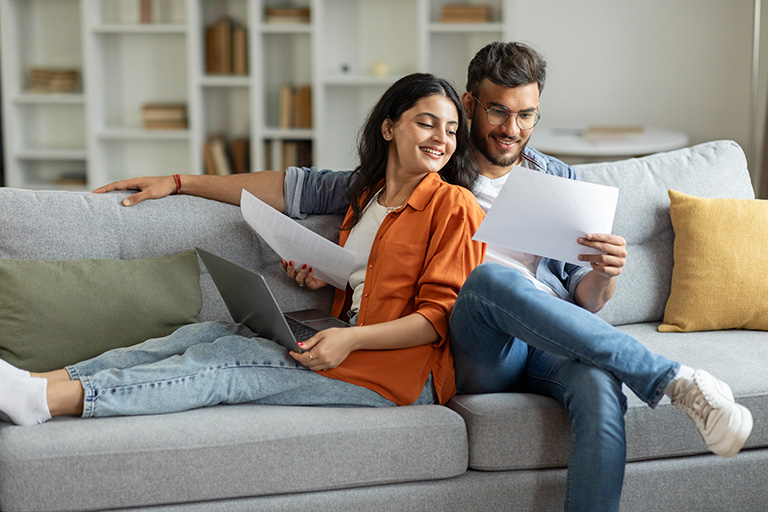 Happy indian couple checking documents, sitting on couch in living room.
