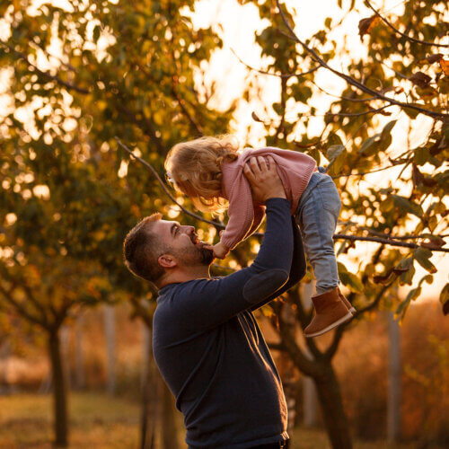 Dad holding his daughter up with trees in the background