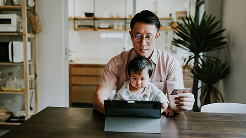 Dad with child at his tablet and debit card from rewards checking account