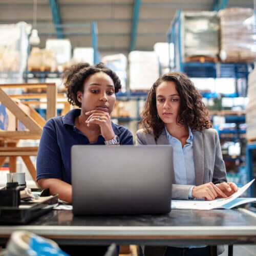 Two warehouse business owners looking concerned at a laptop because of payment fraud